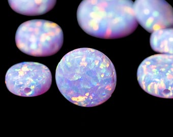 May include: Close-up of several iridescent opal beads in various shapes, including round and oval. The beads have a milky white base color with flashes of blue, pink, and yellow. The background is solid black.