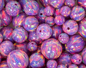 May include: A collection of iridescent purple opal beads in various sizes. The beads have a polished, glossy finish with swirling patterns of pink, orange, and blue. The text "THEOPALDEALER" is at the bottom of the image.