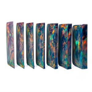 May include: Seven rectangular blocks of dark material featuring a swirling, iridescent pattern of deep blue, green, and vibrant orange hues. Each block is oriented vertically, displaying a smooth, polished surface with a reflective finish.