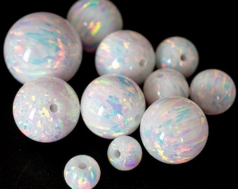 May include: A collection of white opal beads with iridescent swirls and a glossy finish. The beads vary in size and have a hole drilled through the center, suggesting they are for jewelry making or crafting. The background is black.