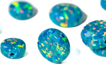May include: Several oval and round blue opal beads with iridescent flecks of yellow, orange, and green. The beads have a glossy finish and some have a small hole drilled through them, likely for stringing.