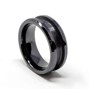May include: A black ring with a grooved central design. The ring has a polished, reflective surface. The design features a central channel, creating a modern and sleek aesthetic. The ring is set against a white background.