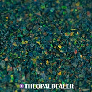 May include: Close-up of a pile of crushed, iridescent opal stones. The stones are primarily dark teal with flashes of green, yellow, and orange. The text "THEOPALDEALER" is at the bottom.