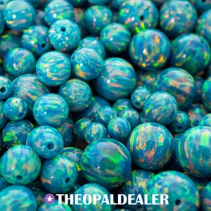 Puede incluir: Primer plano de numerosas cuentas de ópalo azul de varios tamaños. Las cuentas esféricas exhiben patrones arremolinados de color verde, naranja y amarillo. El texto "THEOPALDEALER" es visible en la parte inferior.