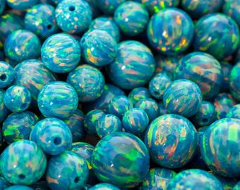 May include: A collection of iridescent blue opal beads in various sizes. The beads have a polished, spherical shape with swirling patterns of green, orange, and yellow. The text "THEOPALDEALER" is visible at the bottom.