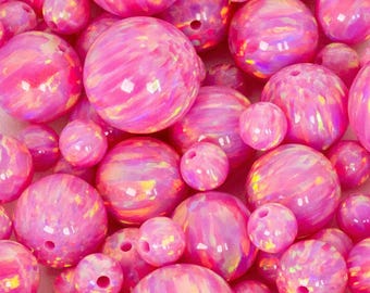 May include: A collection of pink opal beads in various sizes. The beads have a glossy, iridescent finish with swirling patterns. The beads are round with a hole drilled through the center, ready for stringing. The color is a vibrant, saturated pink.