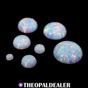 May include: A collection of seven opals with a polished, domed surface. The opals range in size and display a milky white base color with iridescent flashes of pink, blue, and green. The opals are set against a black background. The text "THEOPALDEALER" is at the bottom.