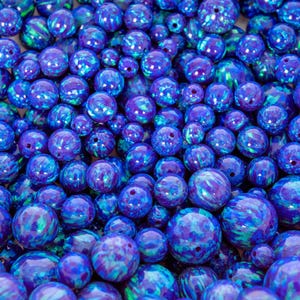 Puede incluir: Una colección de cuentas de ópalo azul y morado. Las cuentas varían en tamaño y tienen un acabado brillante con remolinos de color. Cada cuenta tiene un agujero para ensartar. Ideal para la fabricación de joyas.