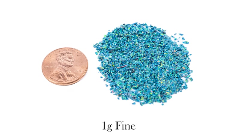 Puede incluir: Un mont&oacute;n de purpurina fina de color verde azulado junto a un centavo estadounidense. La purpurina tiene una calidad iridiscente. El texto "1g Fine" est&aacute; debajo.
