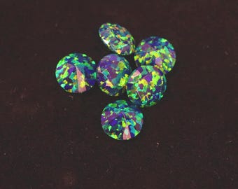 May include: Six round, faceted gemstones in a variety of colours, including blue, green, and purple. The gems are set against a dark brown background. Each gem is approximately 1 cm in diameter.
