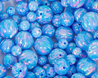 May include: A collection of blue opal beads in various sizes. The beads have a swirling, iridescent pattern with hints of pink and purple. Each bead is drilled with a hole for stringing, perfect for jewelry making.