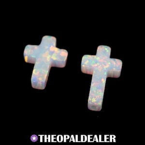 May include: Two white opal cross pendants with iridescent flecks, set against a black background. The crosses have a smooth, polished finish and are illuminated, showcasing their unique colour variations. The text "THEOPALDEALER" is at the bottom.
