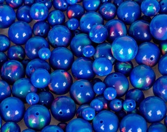May include: A collection of blue opal beads in various sizes. The beads have a glossy finish and display iridescent flashes of color. Each bead has a small hole for stringing. The beads are suitable for jewelry making.