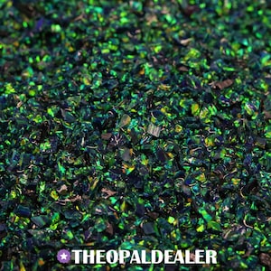 May include: Close-up of a pile of crushed opal pieces. The opal fragments are a mix of green, blue, and black, with a shimmering, iridescent quality. The text "THEOPALDEALER" is at the bottom.