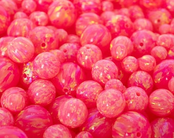 May include: A collection of pink and orange opal beads in various sizes. The beads have a swirling, marbled appearance and are drilled for stringing. The image includes the text "THEOPALDEALER".