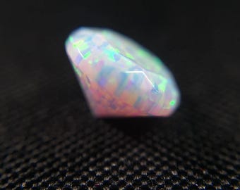 May include: A faceted opal gemstone, oval in shape. The opal exhibits a play of colour, with flashes of green, blue, and pink. The gemstone is set against a dark background, accentuating its iridescent qualities.