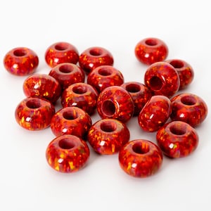 Könnte beinhalten: Eine Sammlung glänzender, rot-oranger Perlen mit einem Loch in der Mitte. Die Perlen haben ein gesprenkeltes, schillerndes Aussehen mit Andeutungen von Gelb und Orange. Diese Perlen eignen sich für die Schmuckherstellung und andere Bastelprojekte.