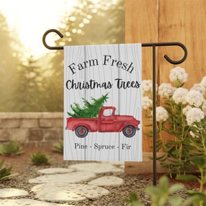 May include: A red pickup truck with a Christmas tree in the bed. The truck is on a white wooden background with the text "Farm Fresh Christmas Trees Pine - Spruce - Fir".