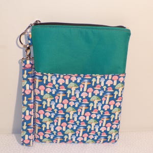 May include: A teal and blue zippered pouch with a wrist strap. The top half is teal, and the bottom half is patterned with colorful mushrooms on a blue background. A silver-colored metal zipper and clasp are visible.