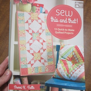 May include: A book titled "Sew this and that!" with a pink and green patchwork quilt on the cover. The book is by Sherri K. Falls and features 13 quick-to-make quilted projects.