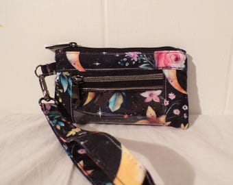 May include: A small black zippered pouch with a floral and moon print. The pouch has a clear plastic window and a detachable strap.