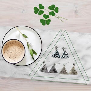 May include: A set of six triangle-shaped earrings with a Celtic knot design. Three earrings are green and three are white.