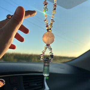 May include: A pink and multi-colored crystal beaded car charm with a large pink crystal in the center and a smaller green crystal at the bottom.