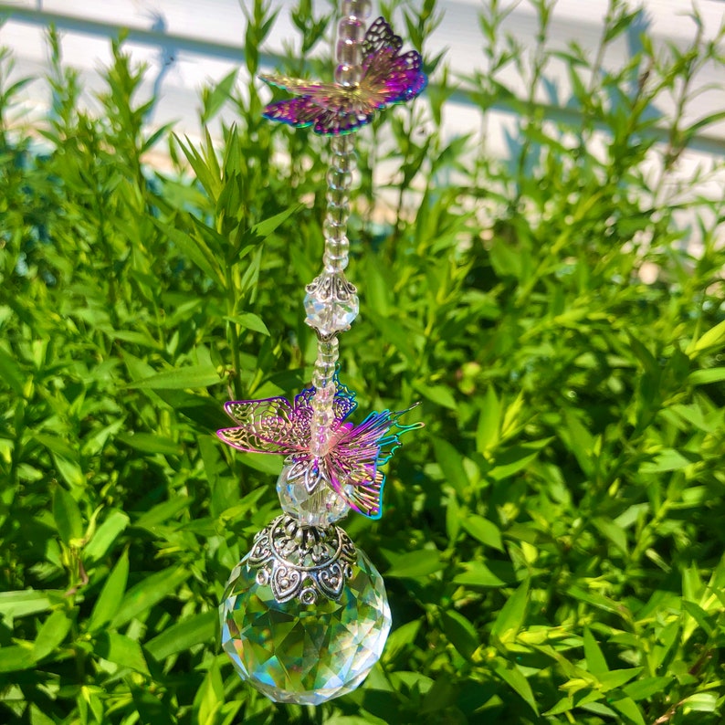 Op de afbeelding: Een kristallen zonenvanger met iriserende vlinders en een gefacetteerde kristallen bol die aan een zilveren ketting hangt.