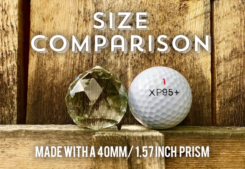 Op de afbeelding: Groottevergelijking van een 40 mm / 1,57 inch kristallen prisma naast een golfbal. De golfbal heeft de tekst "XP95+" erop gedrukt.