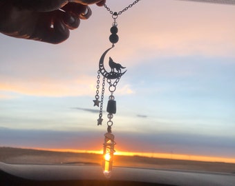 May include: A car charm featuring a silver crescent moon with a wolf howling at the moon, dangling from a silver chain with black beads, stars, and a clear crystal.