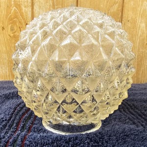 May include: A clear glass lampshade with a diamond-shaped pattern. The vintage light cover is on a blue towel, with a wooden background. The decorative light fixture is a vintage item.