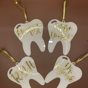 Op de afbeelding: Vier witte tandvormige ornamenten met gouden belettering. De ornamenten luiden "Dentist", "Future Dentist", "Right" en "You got this, keyworker".