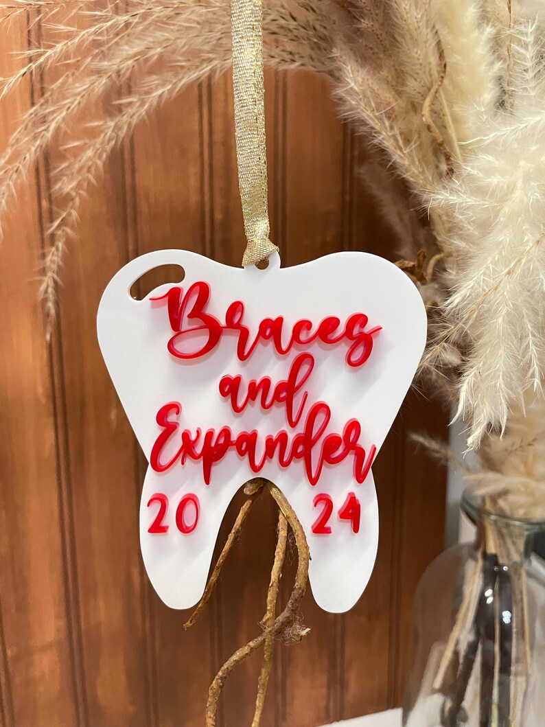 Op de afbeelding: Witte, tandenvormige kerstversiering met rode tekst "Braces and Expander 20 24".