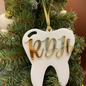 Op de afbeelding: Witte, tandenvormige kerstversiering met een gouden glitterafwerking en de naam "Ryff" in gouden letters.