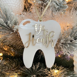 Op de afbeelding: Witte, tandenvormige kerstversiering met gouden glitterlettering die "Dr. Health" zegt.