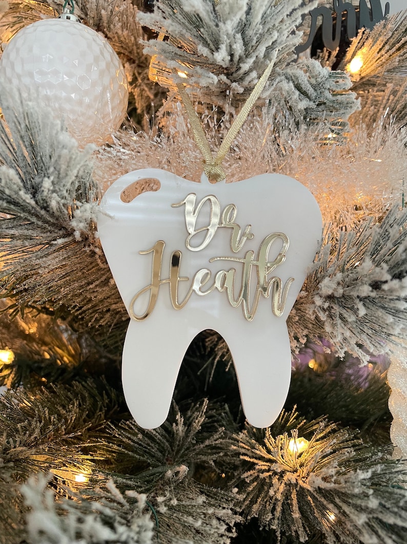 Op de afbeelding: Witte, tandenvormige kerstversiering met gouden glitterlettering die "Dr. Health" zegt.
