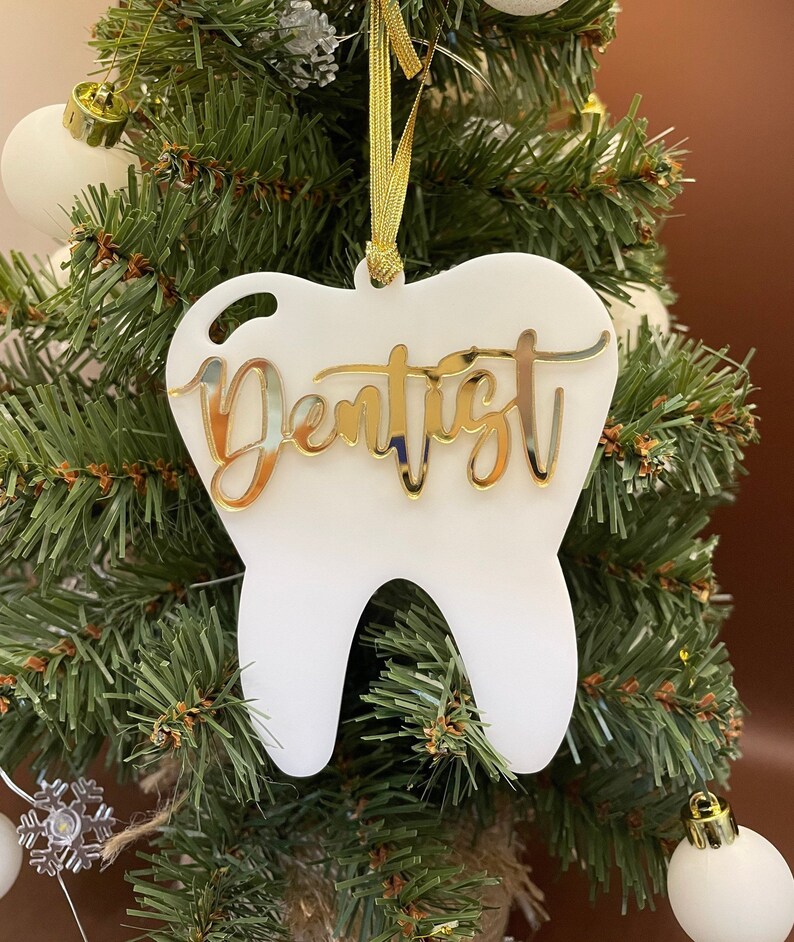 Op de afbeelding: Witte, tandenvormige kerstversiering met het woord "Dentist" in gouden glitterletters.