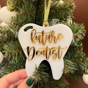 Op de afbeelding: Witte, tandenvormige kerstversiering met gouden glitterlettering die "future dentist" zegt.