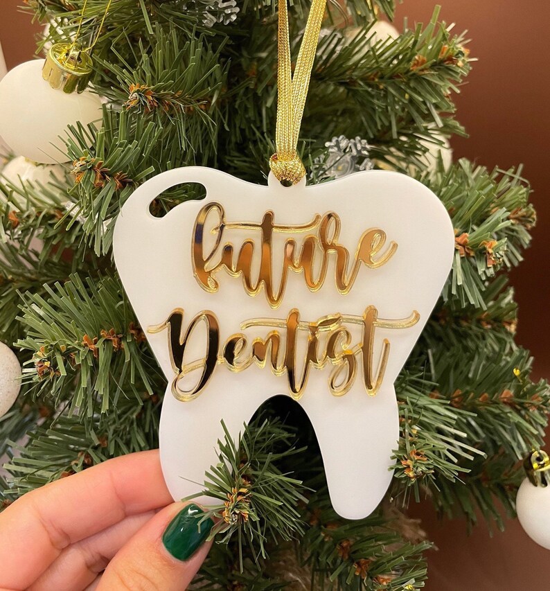 Op de afbeelding: Witte, tandenvormige kerstversiering met gouden glitterlettering die "future dentist" zegt.