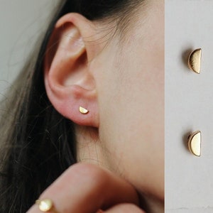 May include: A pair of gold half-moon earrings. The earrings are small and delicate, and they are perfect for adding a touch of minimalist style to any outfit.