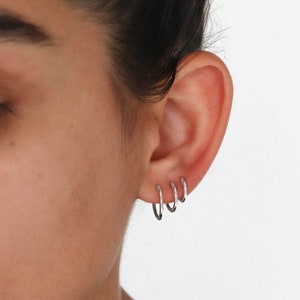 Könnte beinhalten: Eine Person trägt mehrere silberne Creolen im Ohrläppchen.