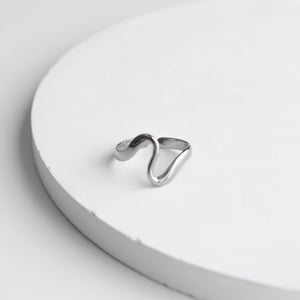 Op de afbeelding: Een zilveren ring met een golvend, abstract ontwerp. De ring ligt op een witte achtergrond.