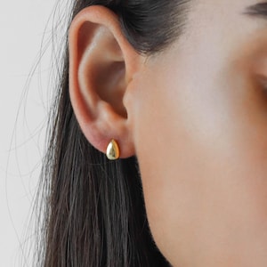 May include: A close-up of a person's ear with a small, gold, teardrop-shaped earring.