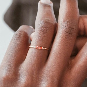 Op de afbeelding: Een delicate gouden ring met drie kleine rode edelstenen in een rij.