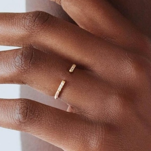 Op de afbeelding: Een gouden ring met een rij kleine diamanten die in de band zijn gezet. De ring is open en heeft een gebogen vorm.