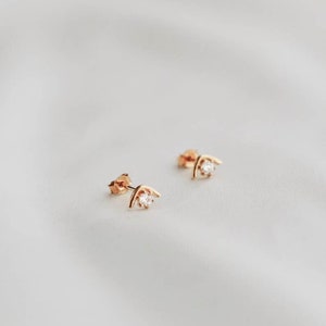 Può includere: Un paio di orecchini in oro con una piccola pietra preziosa trasparente incastonata in un design ad arco curvo.