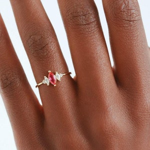 May include: A gold ring featuring a pink marquise-shaped gemstone surrounded by smaller clear gemstones.