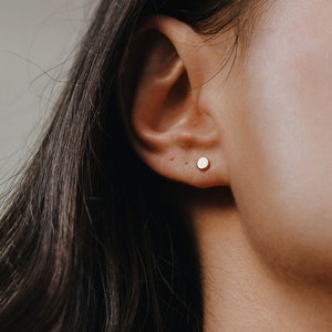 May include: A close-up of a person's ear with a small, round, gold stud earring.