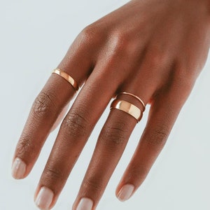 May include: A hand wearing three gold rings. The rings are all different styles and sizes. The hand is resting on a white background.