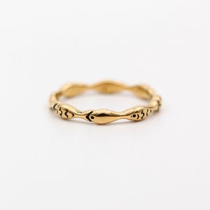 Op de afbeelding: Een goudkleurige ring met een herhalend slangenpatroon. De ring heeft een gladde, gepolijste afwerking en staat tegen een witte achtergrond. Het slangenontwerp heeft kleine, zwarte oogdetails.